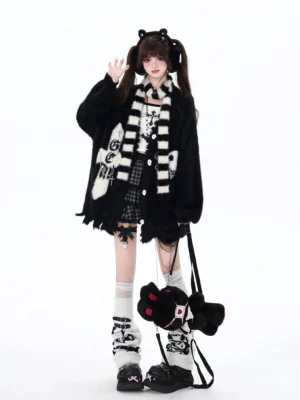 Black Jirai Kei irregular hem cardigan with cross and skull embroidery, paired with black-white striped scarf, worn by female model with twin-tail hairstyle in studio setting