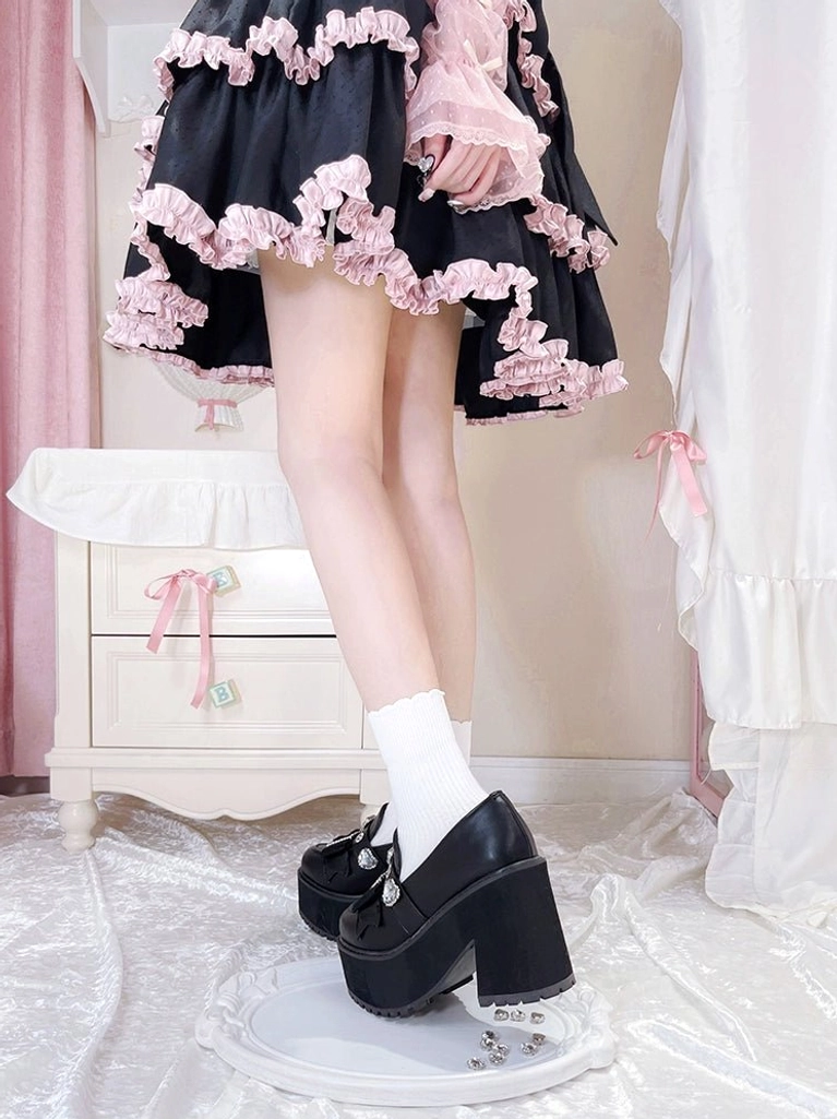 Rear low side view of black Jirai Kei platform loafers with smooth leather upper worn with tiered ruffled skirt on satin bedding in feminine bedroom setting