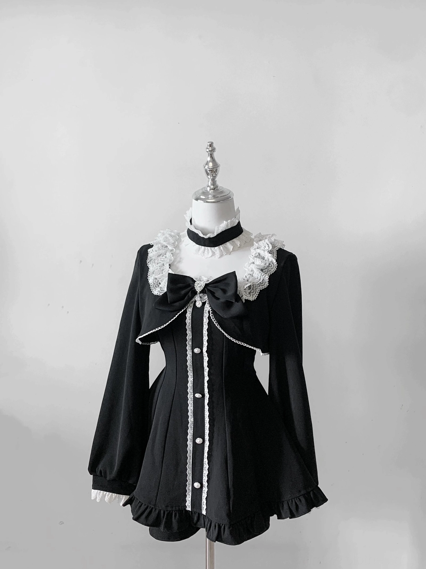 Black gothic Jirai Kei long-sleeve dress with removable chest bow, lace collar, and pearl button trim on mannequin flat display