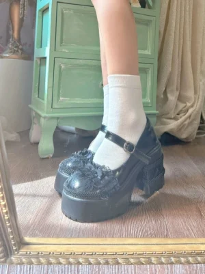 Black patent leather Mary Jane platform shoes with lace toe trim, chunky block heel, white ankle socks, and adjustable ankle strap buckle viewed in mirror reflection, vintage dresser interior backdrop