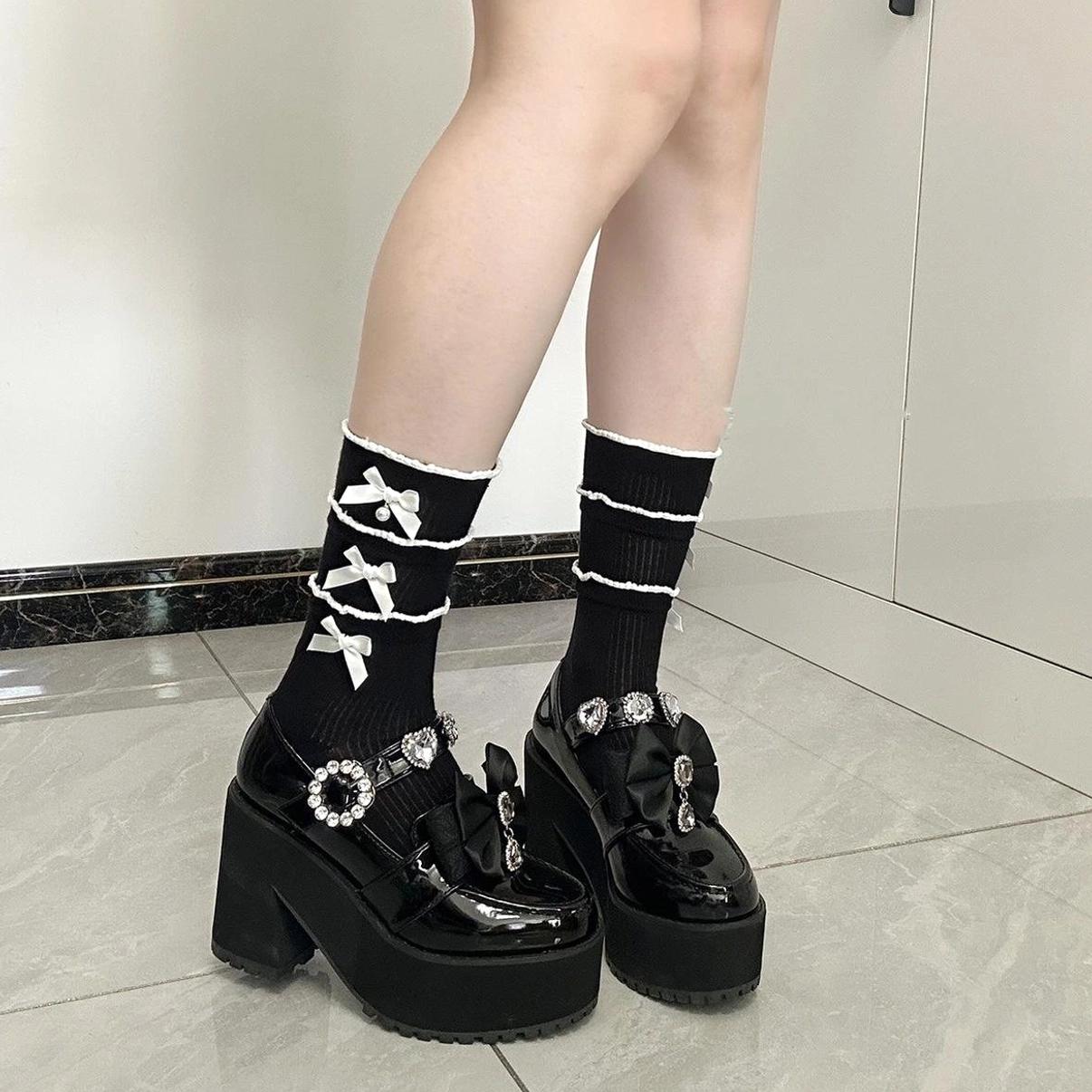 Black mid-calf Jirai Kei socks with white ribbon bows and ruffles worn with platform Mary Jane shoes leg close-up