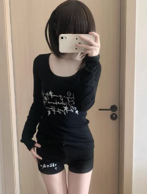 Black Jirai Kei otaku graphic long-sleeve top with thumbhole cuffs and handwritten star pattern design, worn by model in mirror selfie with black shorts, front view