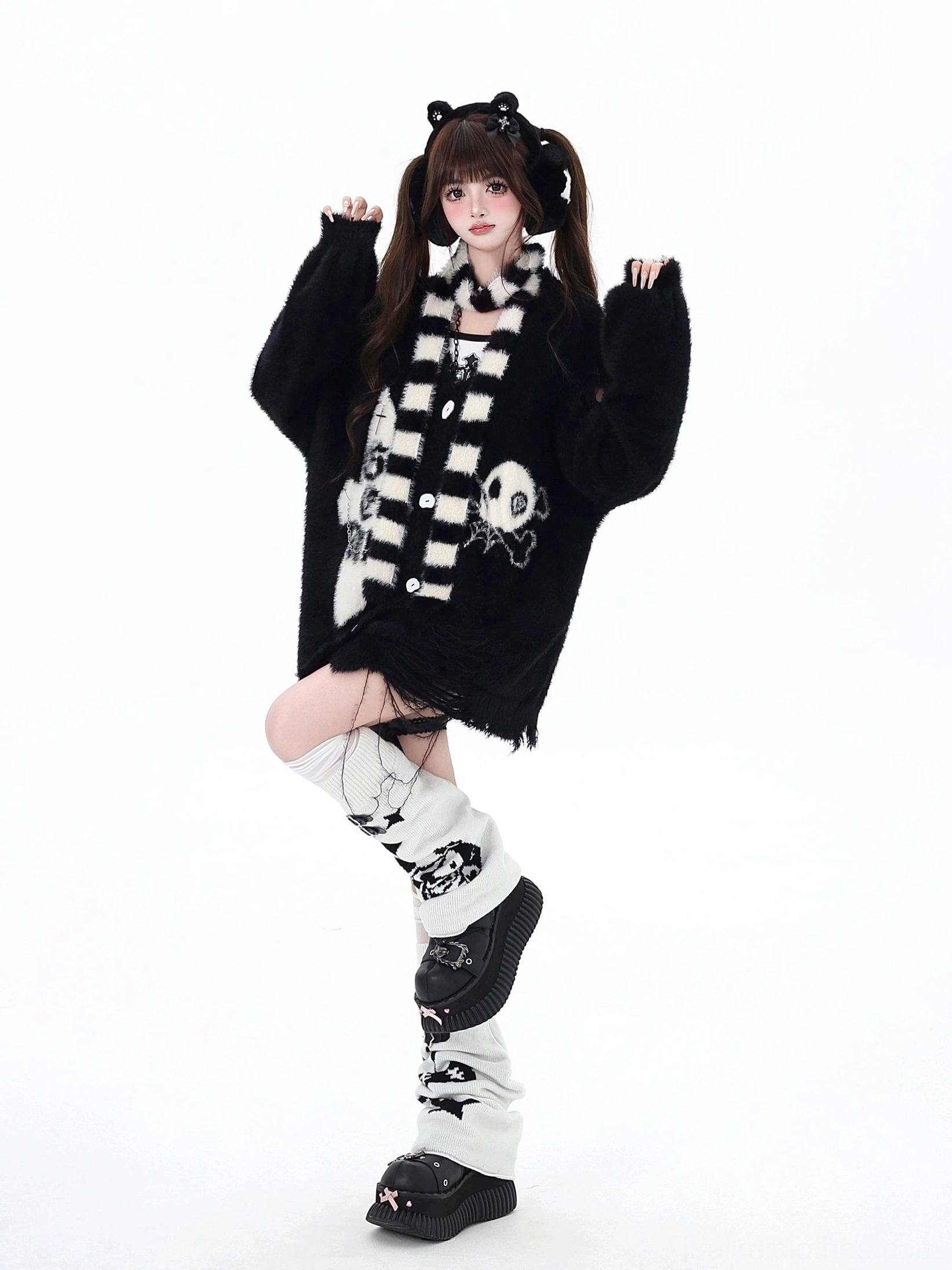Black oversized Jirai Kei cardigan with distressed hem, cross and skull embroidered prints, three-quarter pose with leg lifted, holding coordinated striped scarf