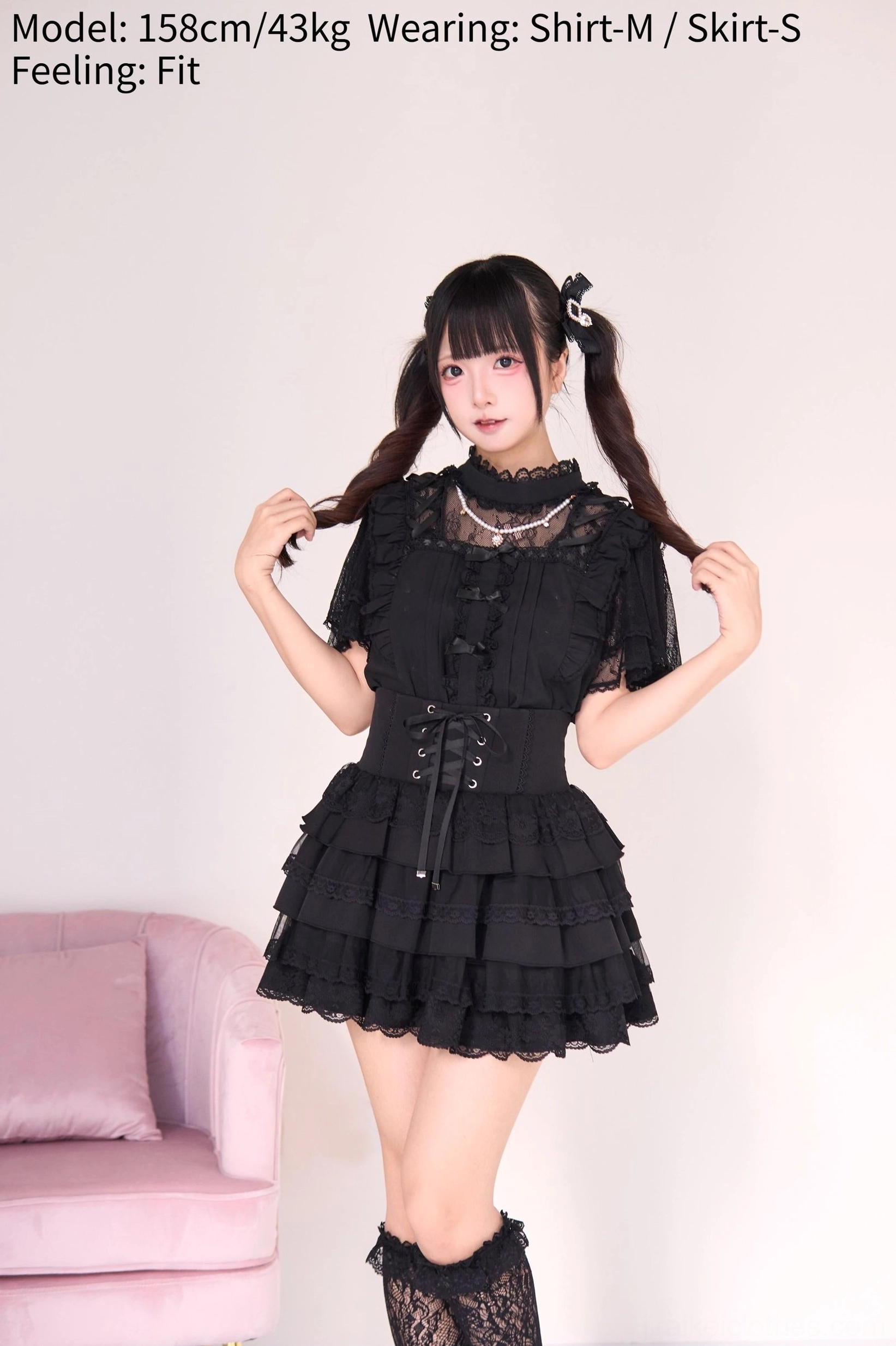 Black gothic lolita jirai kei ensemble with pearl necklace blouse and tiered cake skirt, three-quarter angle view showing lace trim sleeves corset waist and fishnet stockings