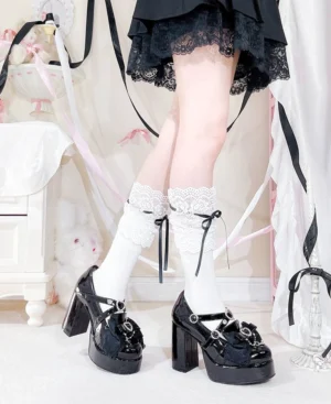 Side-rear view of black patent Jirai Kei high-heel platform shoes displaying chunky block heel, heart rhinestone buckle detail, and lace-trimmed sock styling