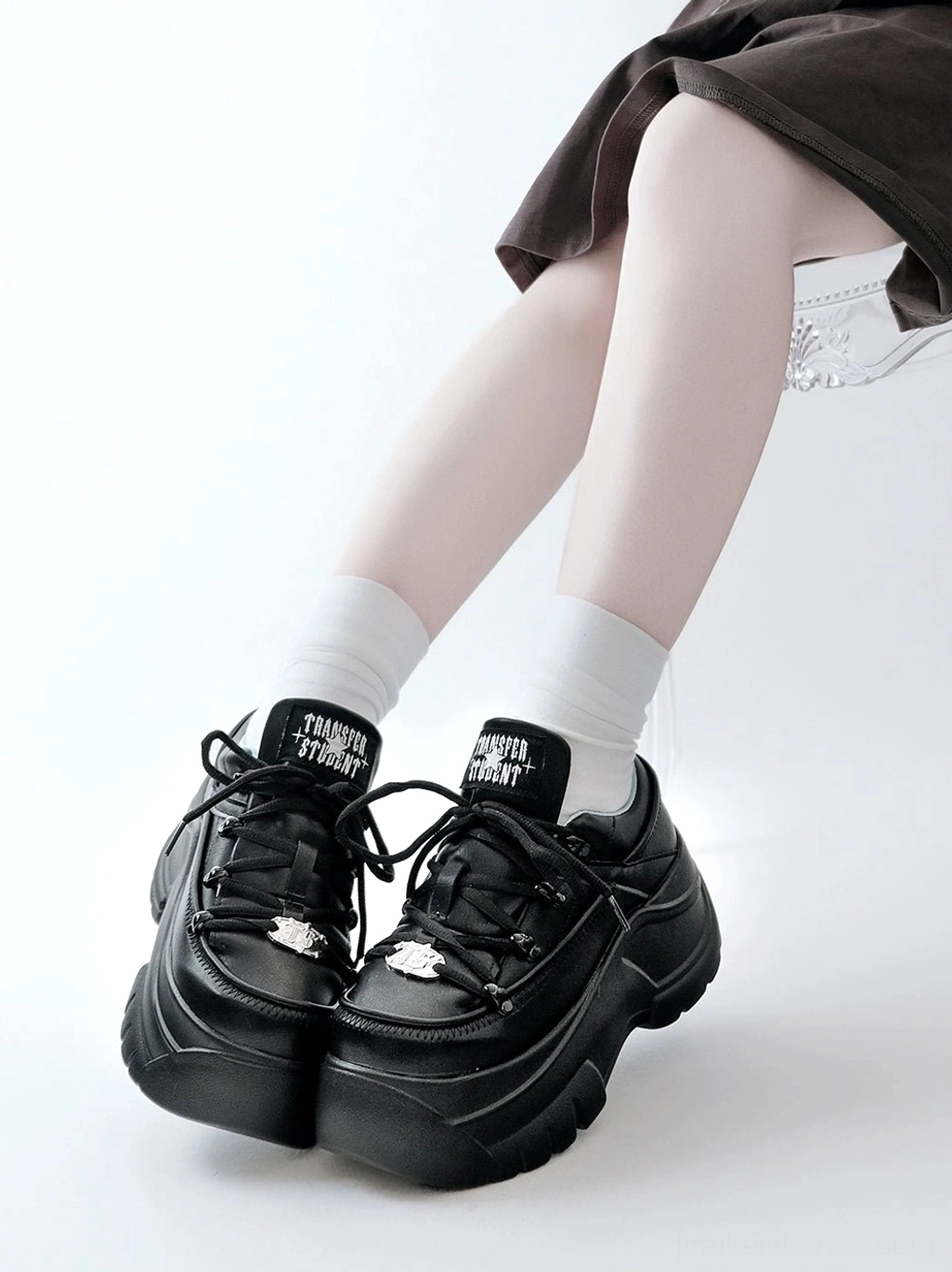 Black thick platform jirai kei sneakers low angle front view with model wearing white crew socks loose outerwear chunky black sole and metal toe ornament