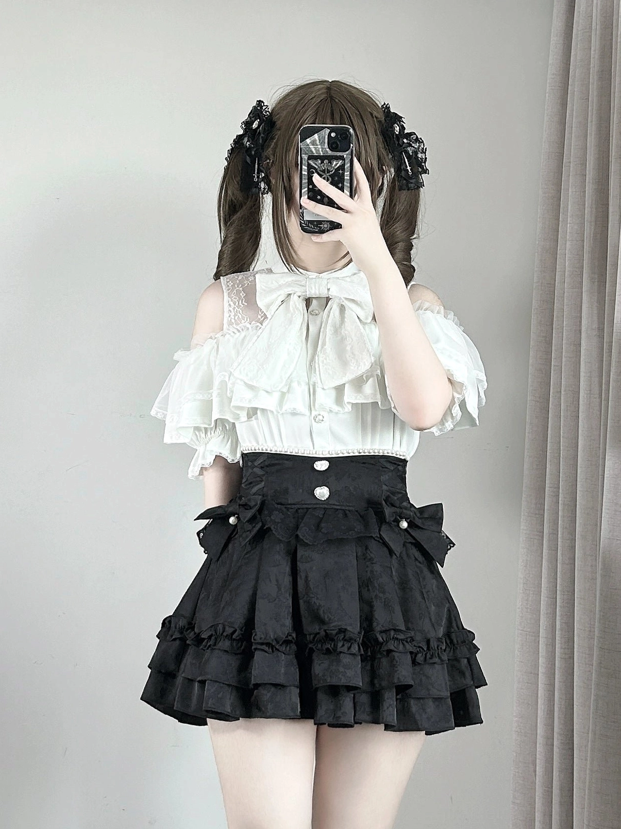 Black jirai kei ruffle skirt with buttoned waist detail and layered hem worn with off-shoulder bow blouse, front mirror selfie view