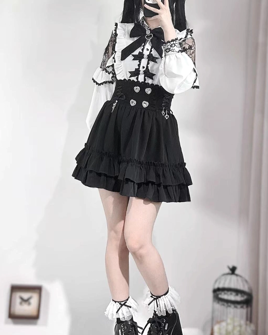 Jirai Kei black skirt with heart rhinestone waist buckles and double-layer ruffle hem, worn with lace panel sleeves, oblique front mirror selfie perspective showcasing flounce movement