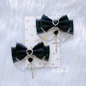Black lace jirai kei hair clip with double-layer bow, heart-shaped black rhinestones, and delicate metal chains displayed on white plush backdrop with heart pattern card