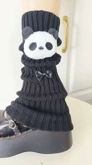 Black ribbed knit leg warmers with 3D panda ornament and small black bow detail close-up on model leg with platform shoe, Jirai Kei fashion aesthetic