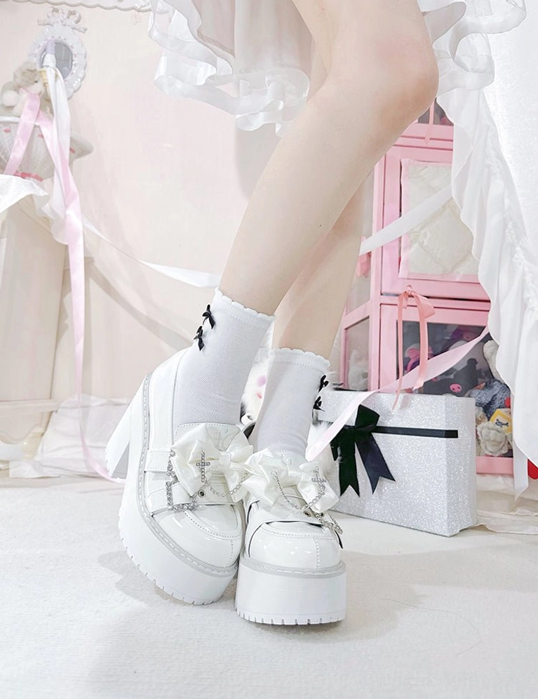 Black patent leather Jirai Kei platform shoes back view of feet showing glossy leather shine, rhinestone decorative elements, chunky platform heel, white socks, and black ruffled skirt base