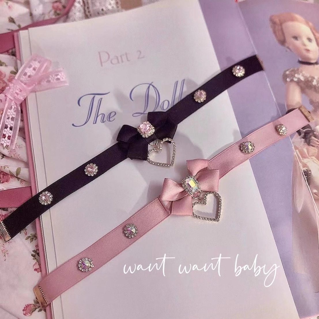 Pair of black and pink bow rhinestone chokers displayed on vintage book backdrop highlighting gold-tone hardware and rhinestone embellished straps