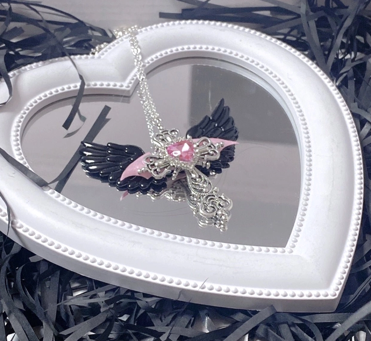Black and pink Jirai Kei devil-style winged cross necklace with pink heart gem and pink fabric accents on white heart mirror