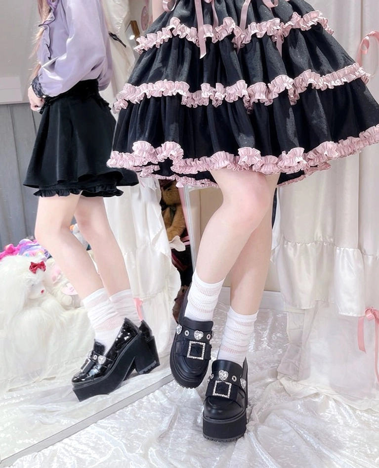 Two models wearing black Jirai Kei platform loafers with ruffled girly skirts in bedroom mirror setting showing chunky platform sole design