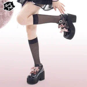 Side profile of black platform loafers with pink satin velvet bow and rhinestone embellishments, worn with black knee-high socks on model