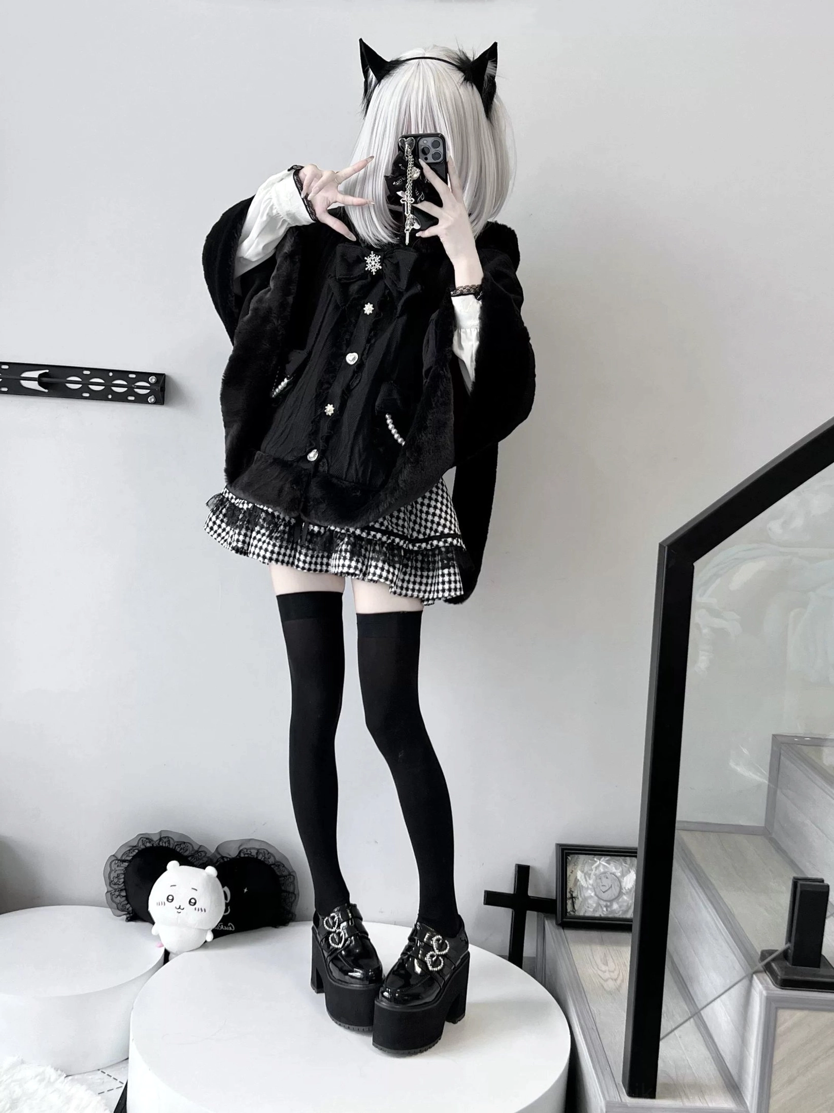 Front mirror selfie of black cat-ear themed fleece cape coat worn with plaid mini skirt, black front button design, and indoor studio background