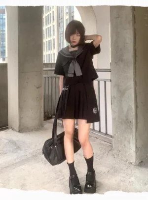Short-sleeve black sailor JK uniform with mini pleated skirt, leather tote bag, platform shoes, styled at concrete building angle view