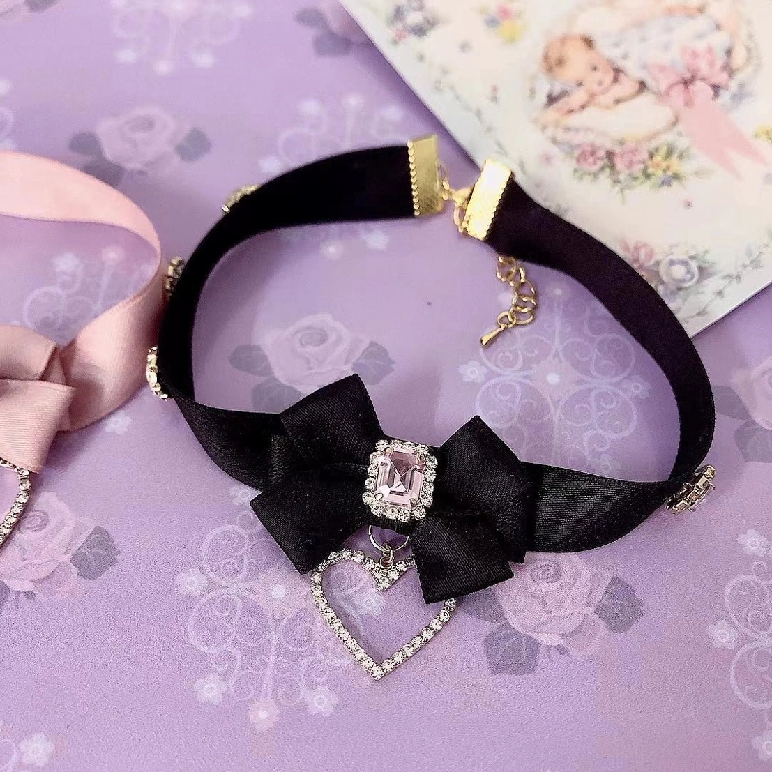 Black satin ribbon bow rhinestone choker necklace with adjustable clasp and sparkling heart pendant detail photographed on vintage purple backdrop