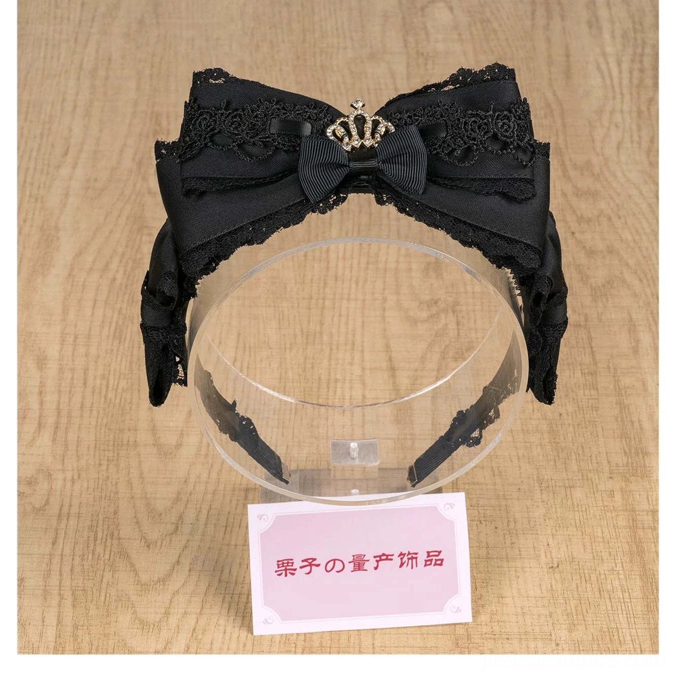 Black satin lace bow headband with thick lace trim and rhinestone crown on stand flat view