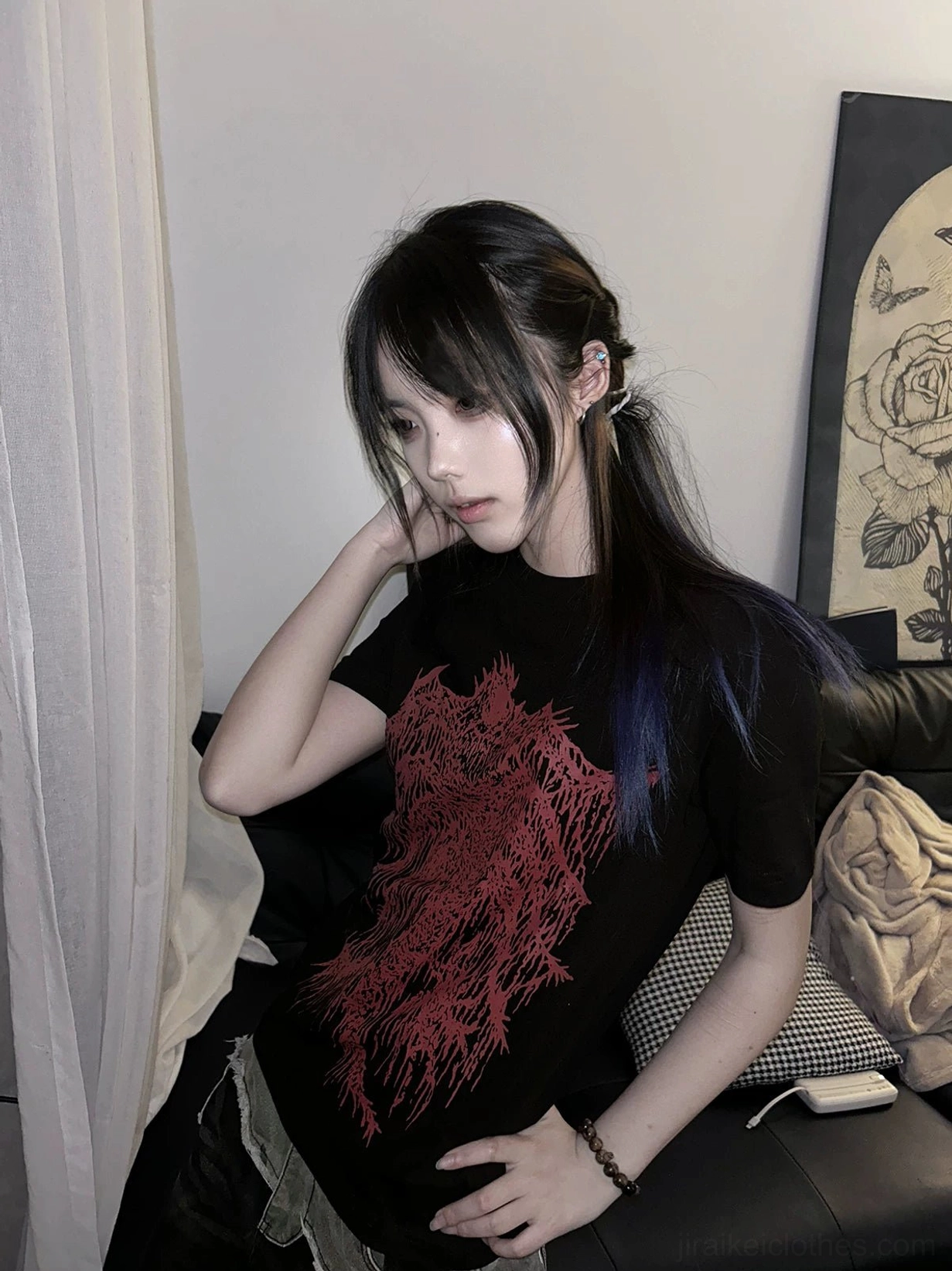 Black t-shirt with red gothic graphic print on front, female model sitting on sofa half-side indoor view, dark subculture fashion style