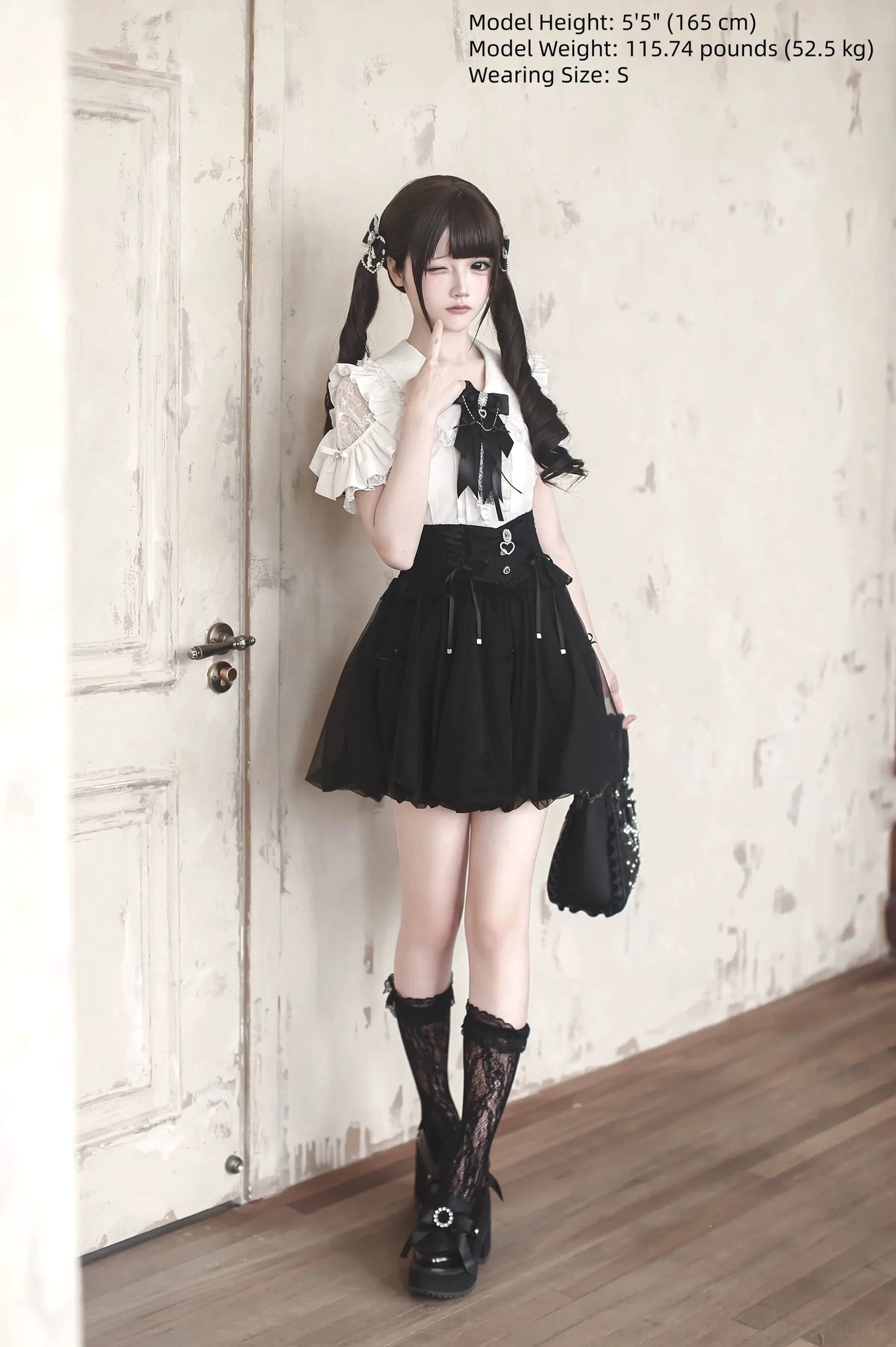 Black and white Jirai Kei two-piece outfit featuring bubble skirt with ruffled blouse and black bow, model with twin tails and handbag indoor door background