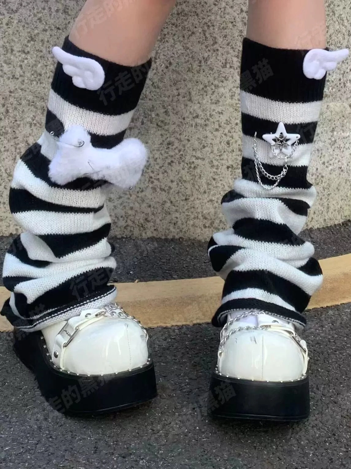 Outdoor close-up of black and white striped leg warmers with angel wings fluffy decoration and star chain charm details with black-soled white platforms