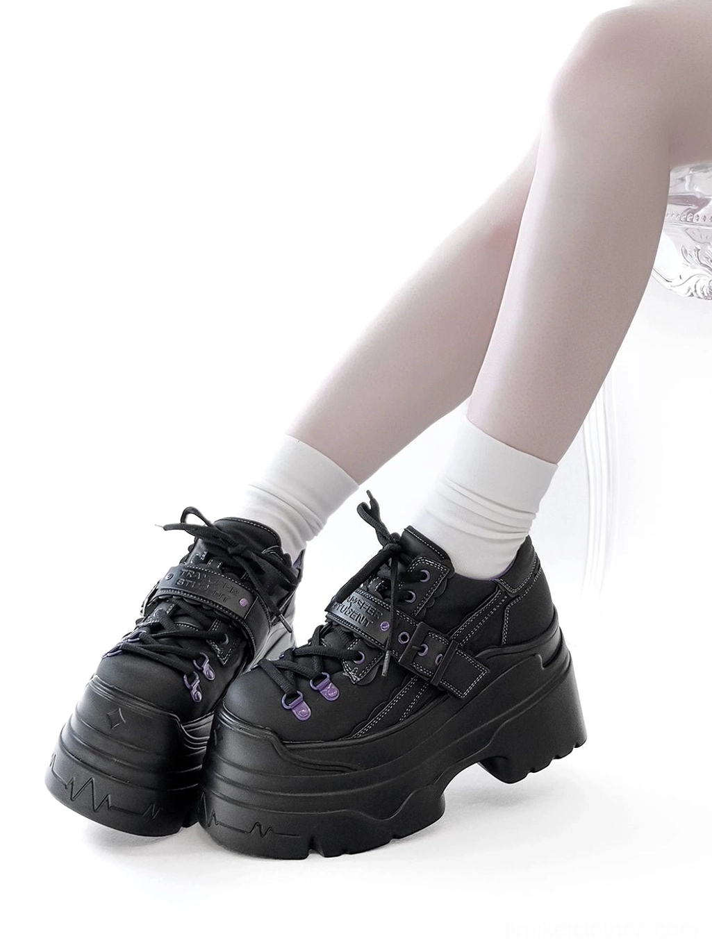 Black Y2K jirai kei platform shoes side view on female model wearing white socks, chunky platform sole with strap buckle and purple eyelet details