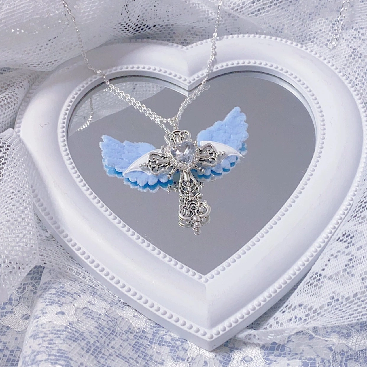 Gradient blue angel wing cross necklace with clear heart rhinestone and silver ornate cross on white heart mirror with lace background