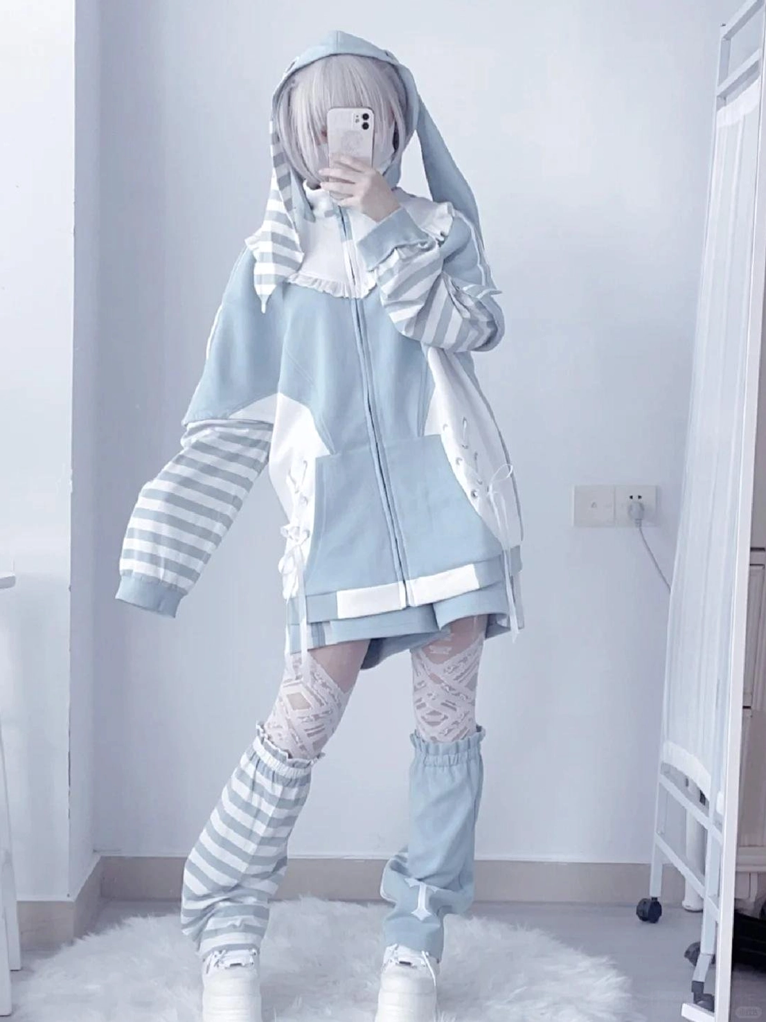 Mirror full-body shot of blue Tenshi Kaiwai hoodie streetwear set with removable striped sleeves, bunny ear shaped hood, and striped leg warmers on silver grey hair model