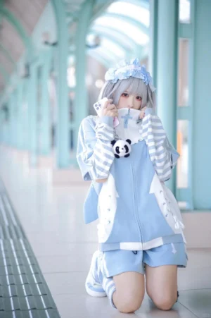 Blue Tenshi Kaiwai hoodie full-body front view worn by silver grey hair model kneeling indoors, featuring striped sleeves, ruffled collar, and cute panda pendant accessory