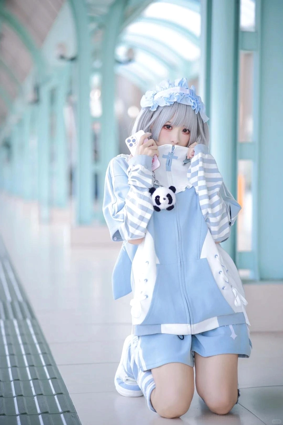 Blue Tenshi Kaiwai hoodie full-body front view worn by silver grey hair model kneeling indoors, featuring striped sleeves, ruffled collar, and cute panda pendant accessory