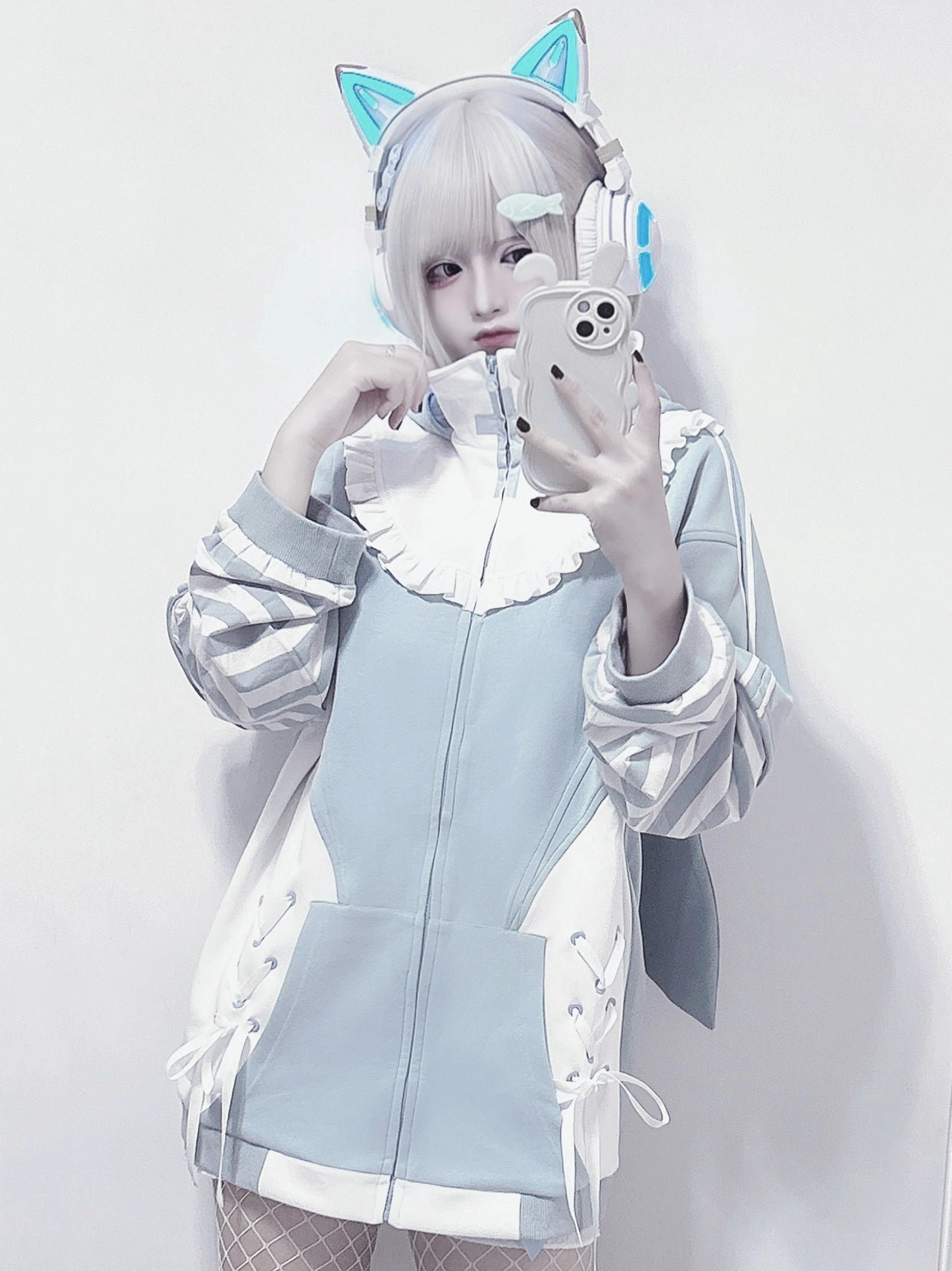 Close-up front selfie of blue zip-up Tenshi Kaiwai hoodie jacket with ruffled collar, striped sleeves, lace-up side details, front pocket on model with cat ear headphones