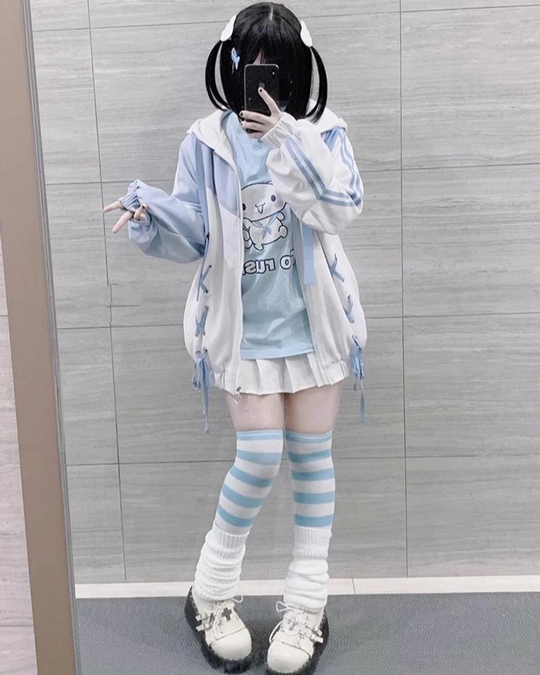 Blue-white Tenshi Kaiwai lace-up hooded jacket full-body mirror view with printed inner tee, pleated skirt, and striped leg warmers on model in corridor
