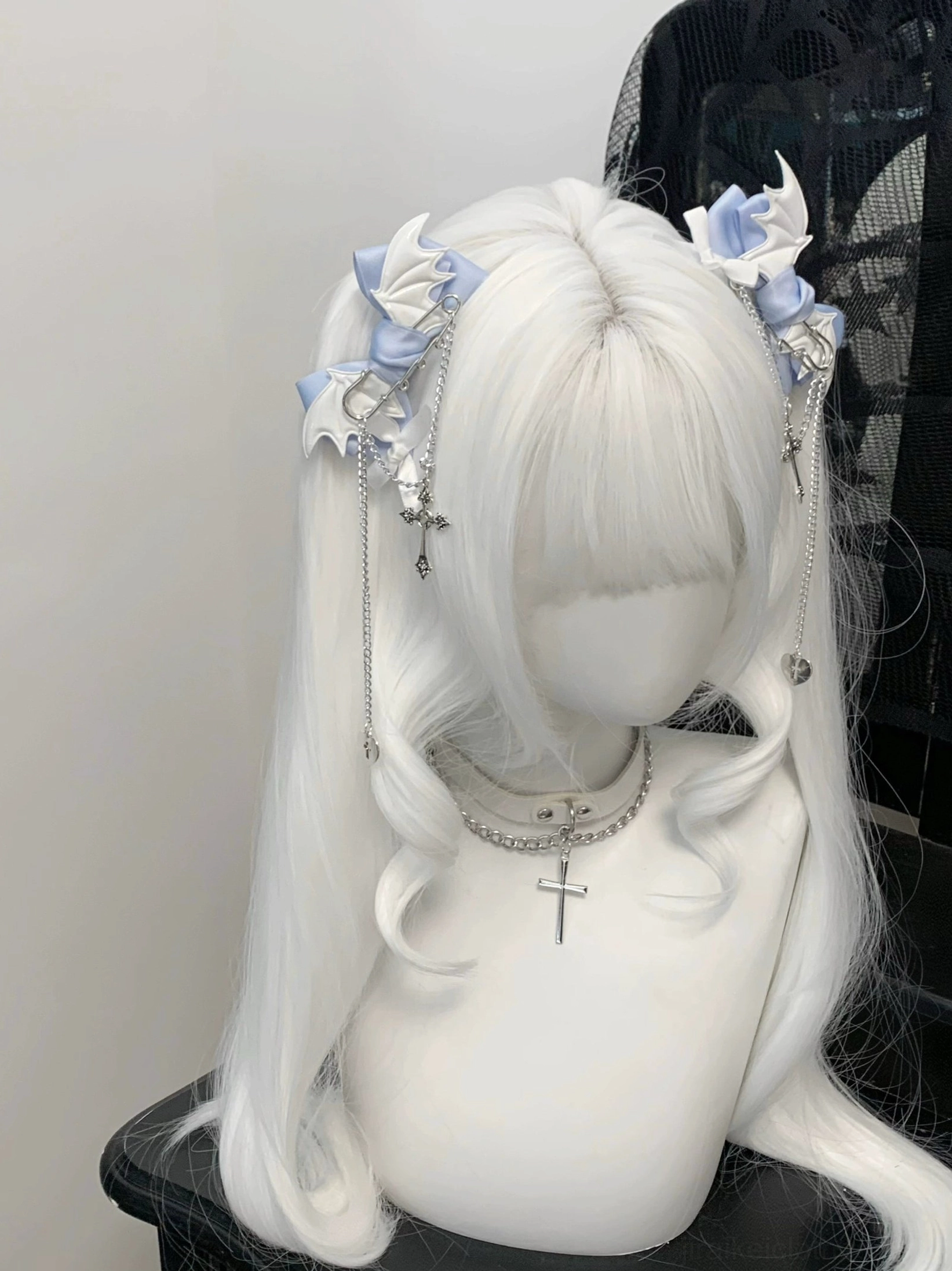 Pair of blue-white winged bat bow hair clips displayed symmetrically on white curly wig mannequin with cross choker - direct front view of Jirai Kei hair accessories