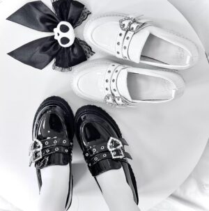 Black and white patent leather platform loafers with studded straps and heart rhinestone buckles top-down view on white round table