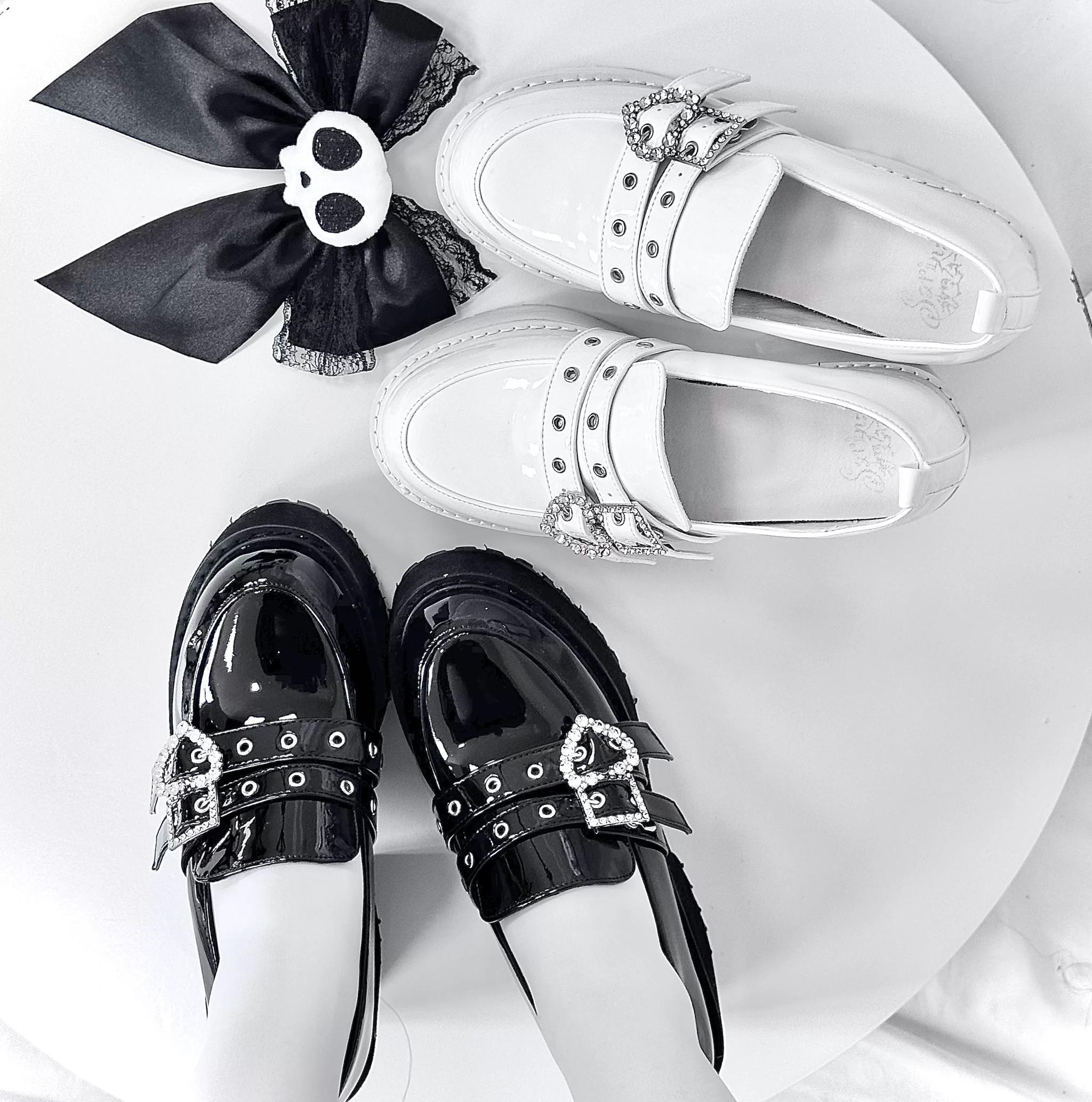 Black and white patent leather platform loafers with studded straps and heart rhinestone buckles top-down view on white round table
