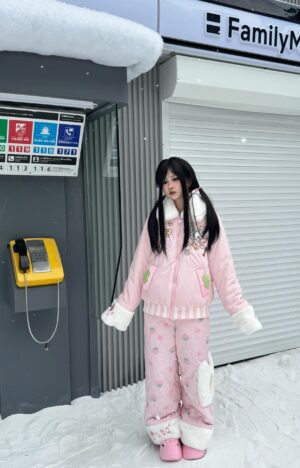 Pink Jirai Kei strawberry padded winter coat with white fuzzy collar and cuffs, front three-quarter view on female model in snowy Japanese street scene with FamilyMart storefront