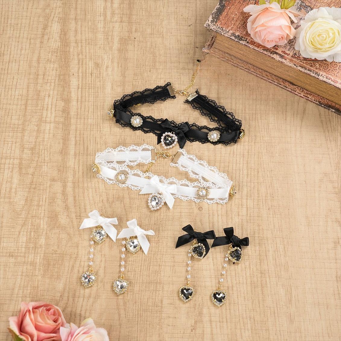 Black lace and white satin Jirai Kei choker set with dangle earrings arranged on wooden desktop surrounded by pink roses