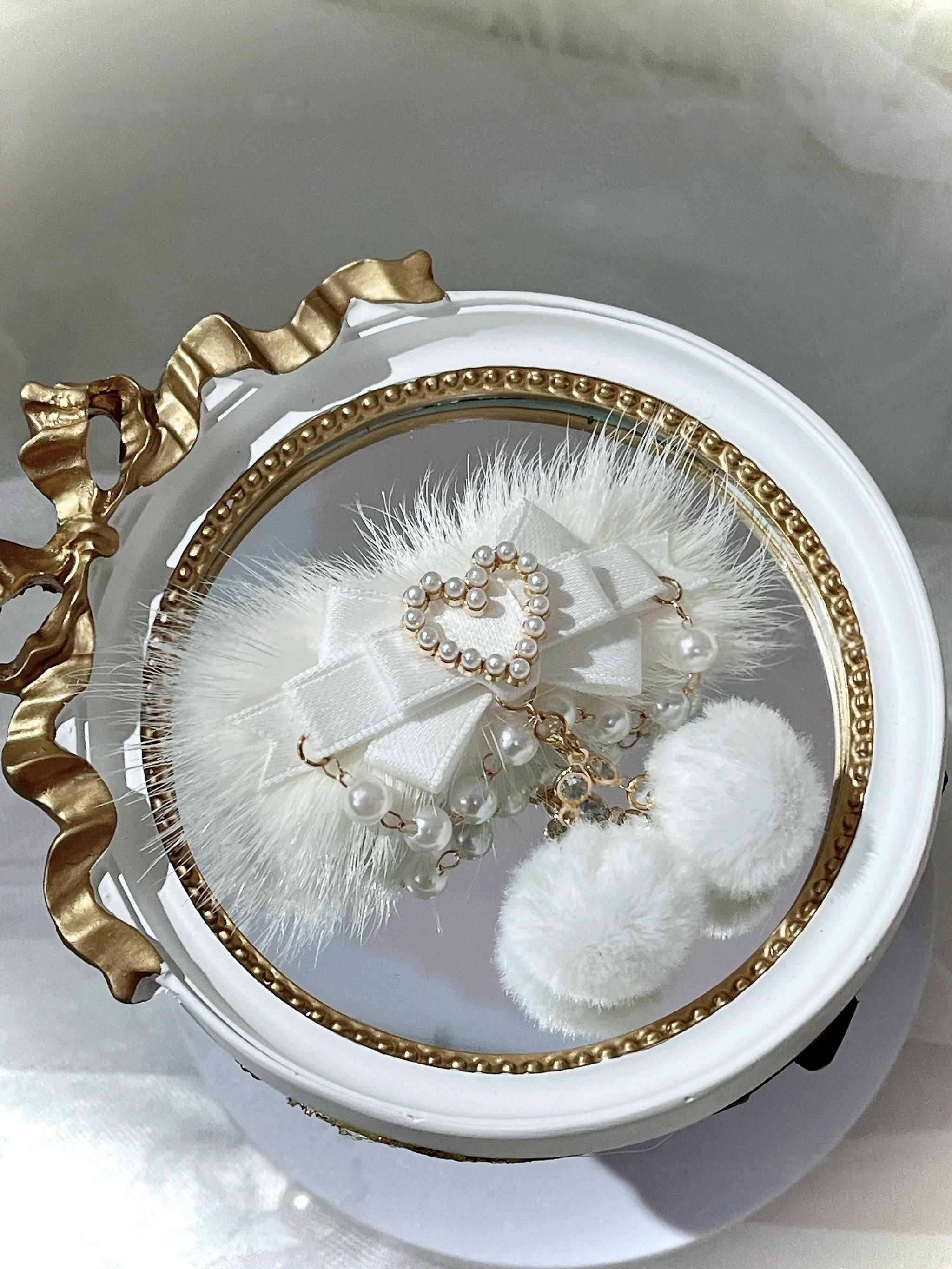 White satin ryousangata pom-pom hair clip with fluffy fur trim and pearl heart pendant on vintage gold-edged white tray, jirai kei lolita hair accessory flat lay styling