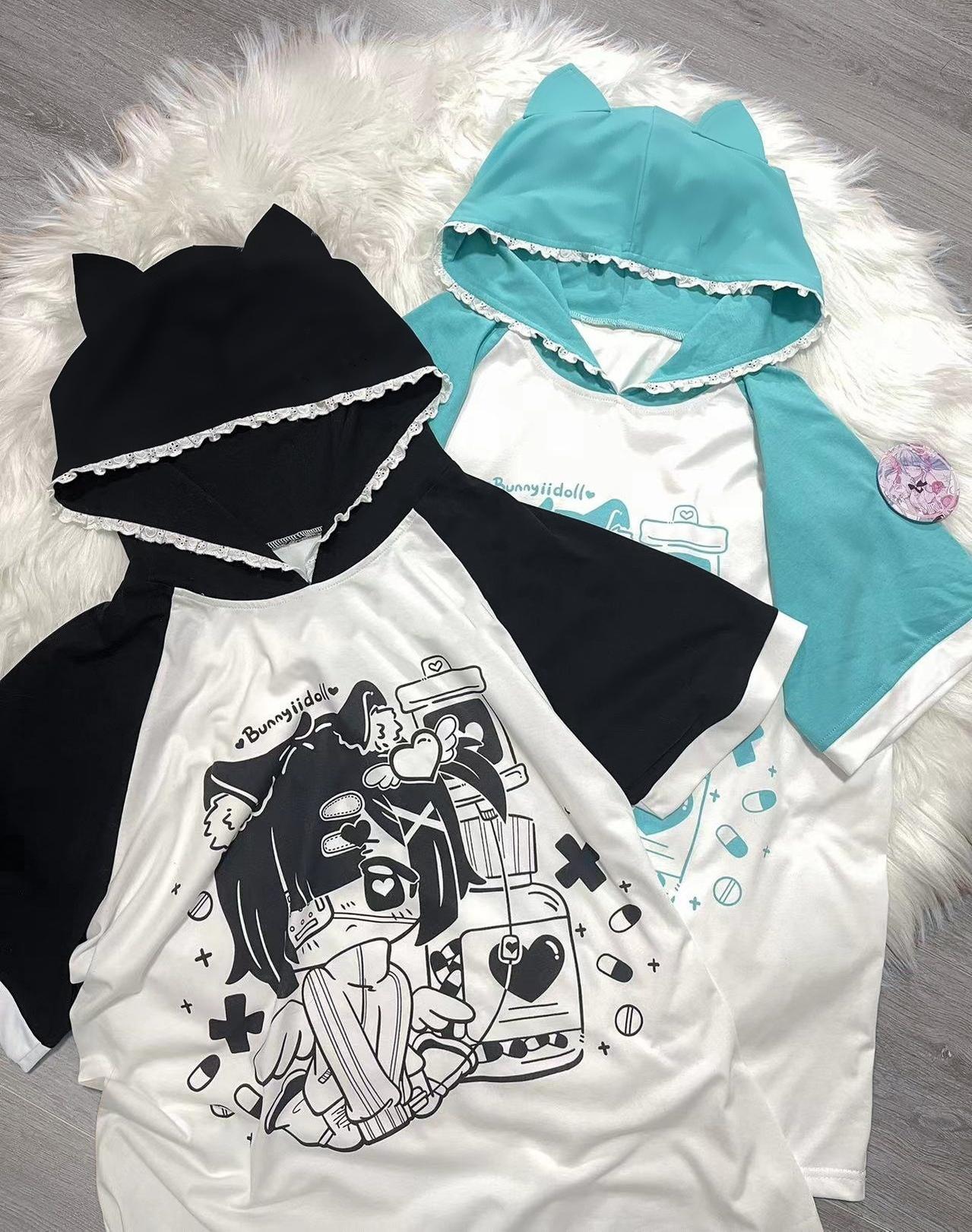 Flat lay product display showing two-color options of cat ear hooded anime graphic tees in black-white and cyan-white, lace-trimmed hood details, decorative badge, jirai kei fashion