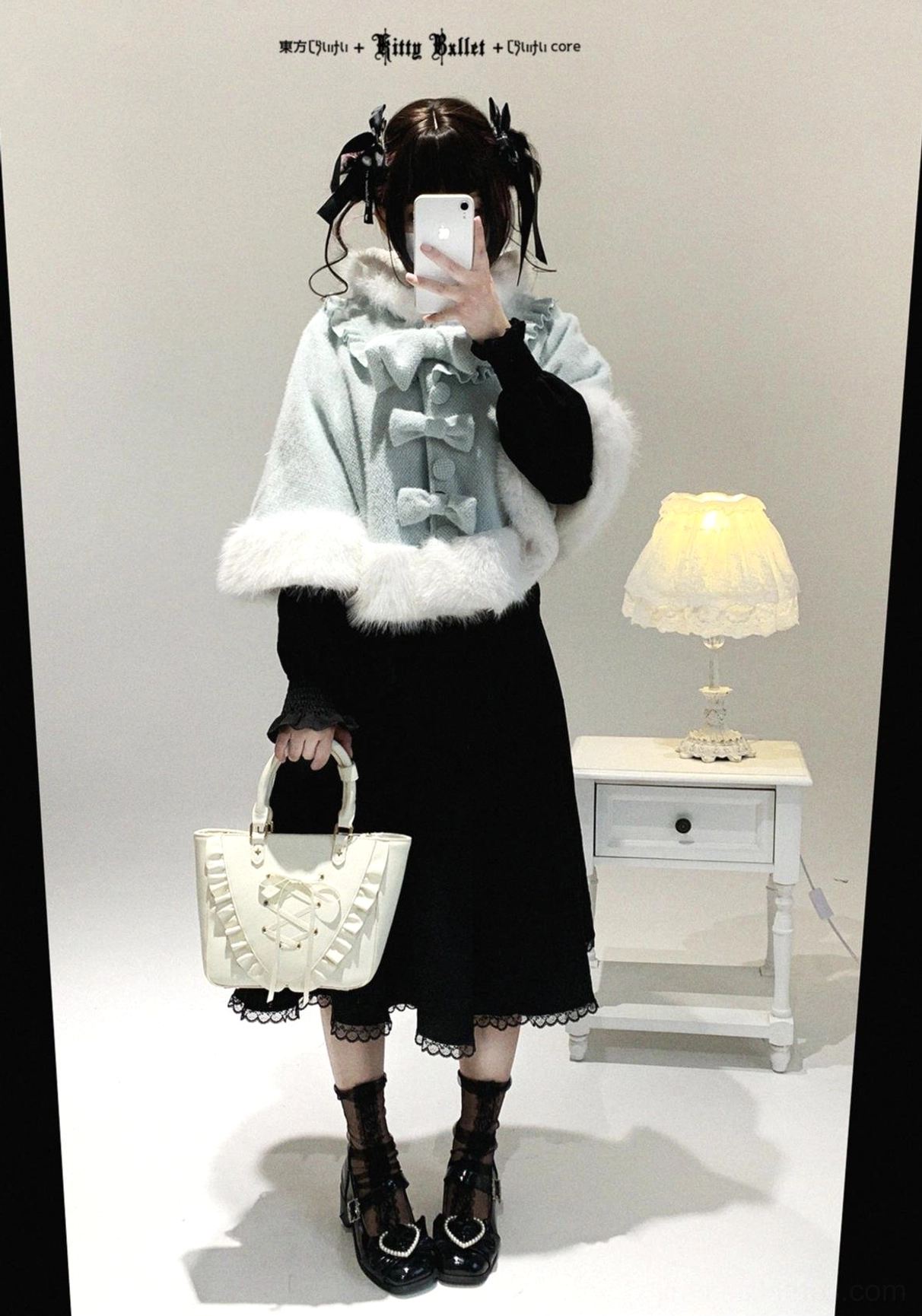 Single model front full-body shot in black midi dress with light blue cat-ear cape, white fuzzy trim, detachable front bow, paired with ruffled handbag