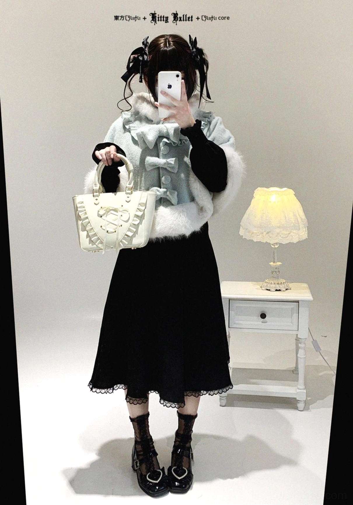 Model wearing light blue cat-ear hooded cape over black dress indoors, showcasing white fur trim and front bow decoration in bedroom setting