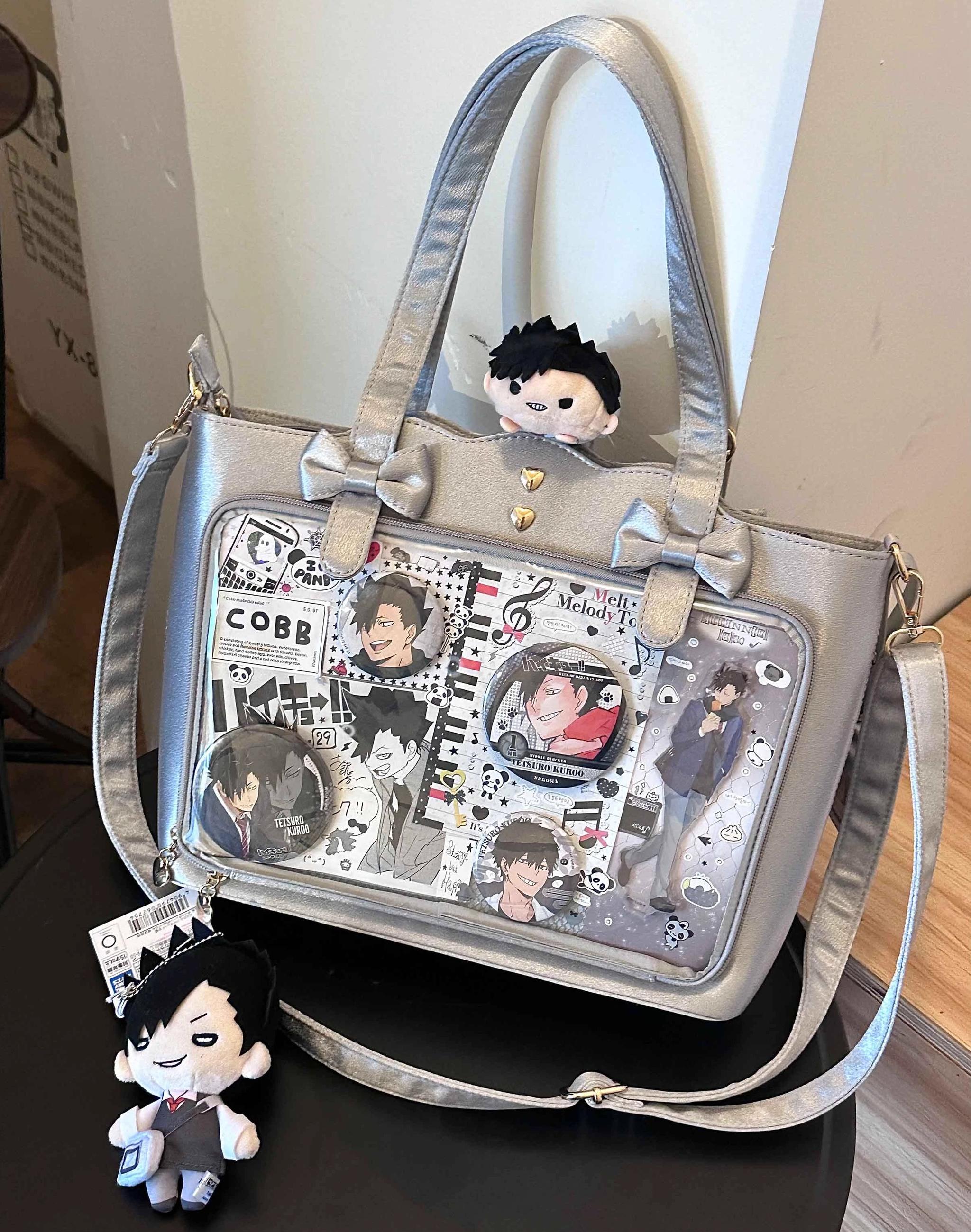 Silver gray Jirai Kei ita bag front overhead display view on tabletop setting, showcasing heart-shaped metal studs, anime pin window display, decorative bow details, dual shoulder straps, and sturdy construction