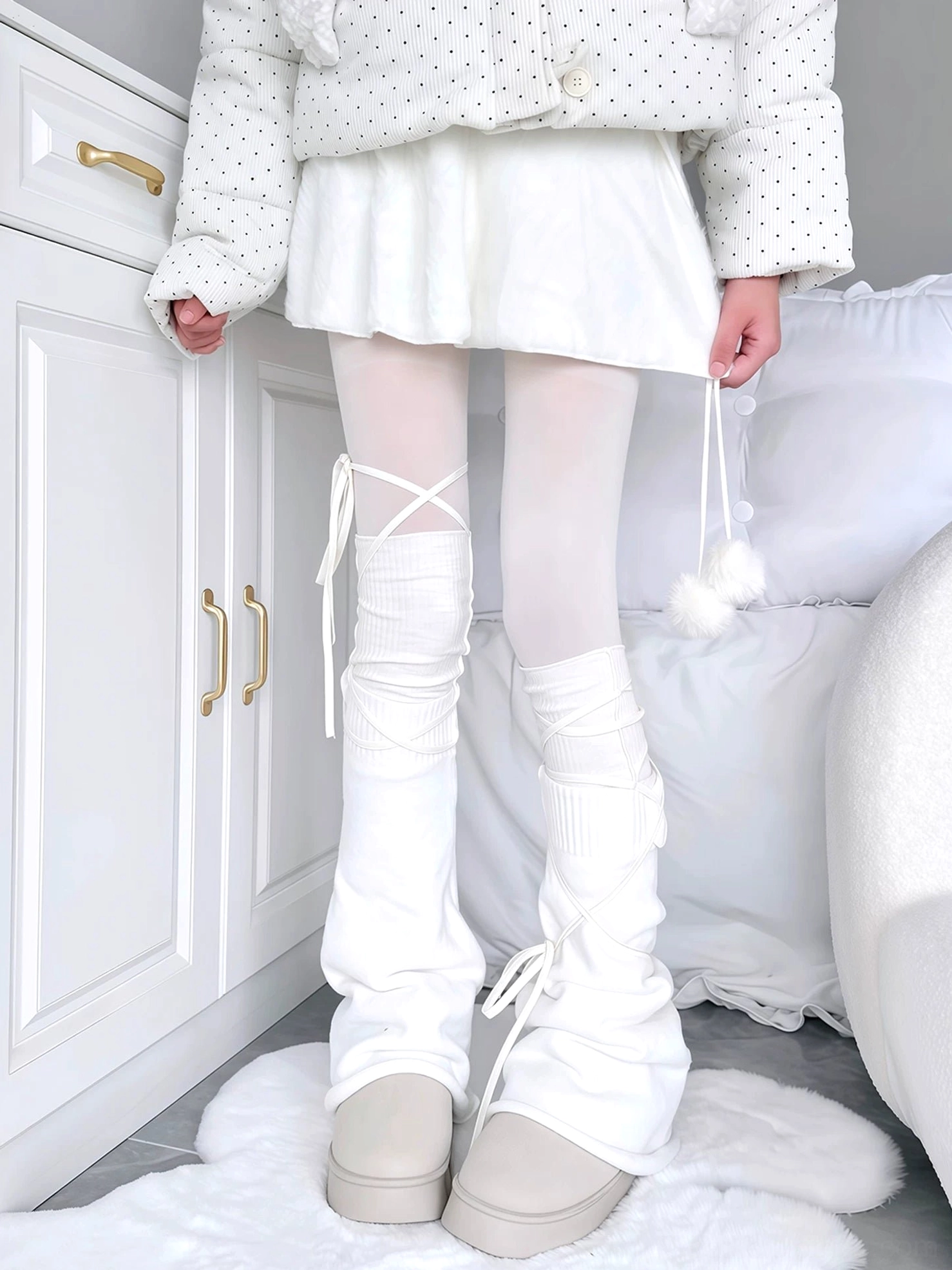 Cross-lace slouchy white leg warmers with front ribbon ties pure white knitted fabric loose stacked fit paired with white tights beige platform shoes bedroom setting low-angle view