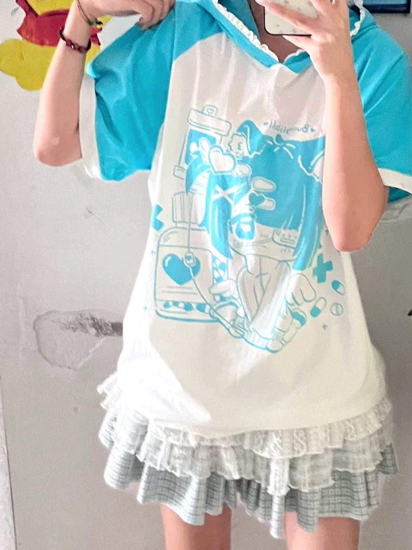 Female model wearing light blue cyan yami kawaii cat ear hooded graphic tee with lace-trimmed hood and anime character print, upper-body mirror selfie showing raglan sleeve design