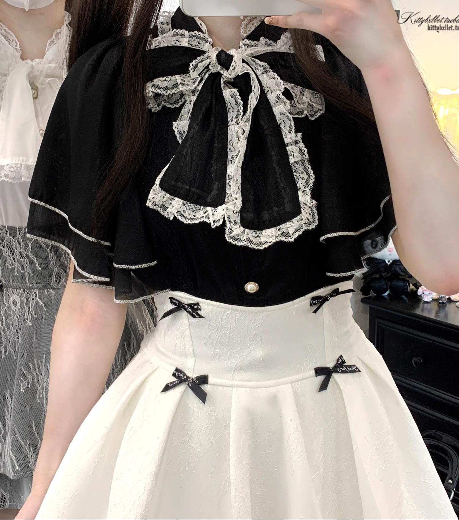 Upper body close-up of female model in black lace blouse paired with white double-layered jirai kei skirt, featuring ruffled sleeves and black bow decorations on skirt