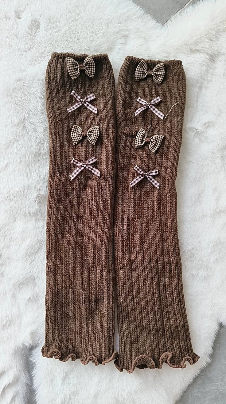 Dark brown ribbed knitted Jirai Kei long stockings with multiple small bows and ruffled cuffs, flat lay on white fur rug