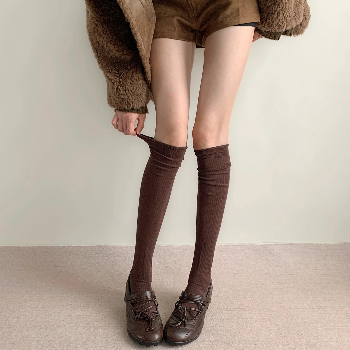 Dark brown calf-length ribbed socks worn with loafers cropped fuzzy coat studio carpet side view