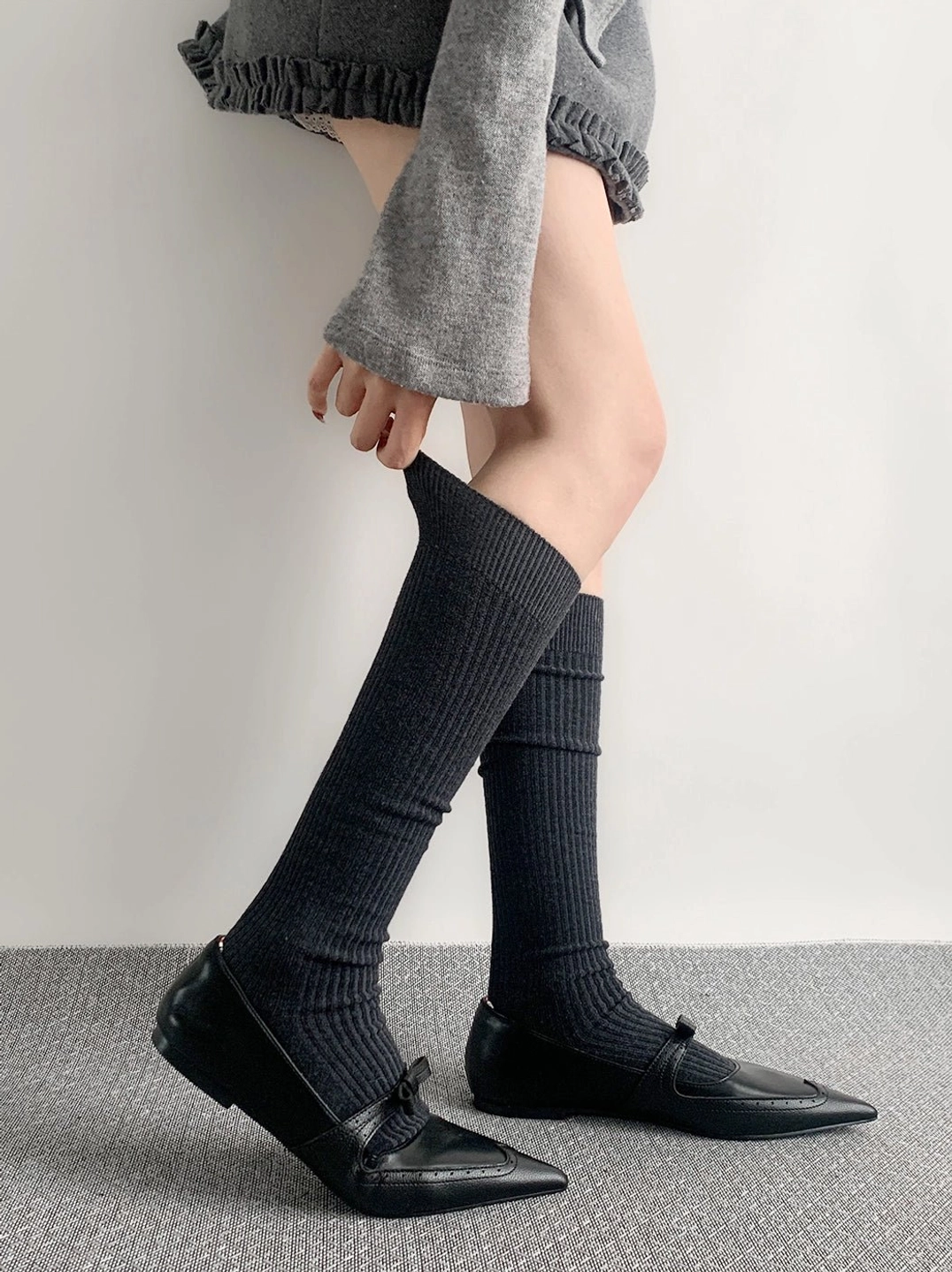 Dark grey calf-length ribbed socks worn with loafers cropped grey top studio styling side angle