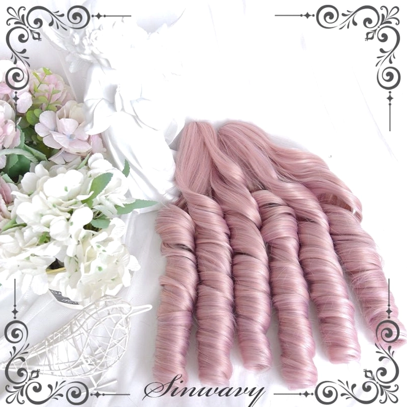 Top-down flat lay view of dusty pink Roman curl hair bundles showing large tight ringlet curls and stacked loose styling arrangement with flower and angel ornament background